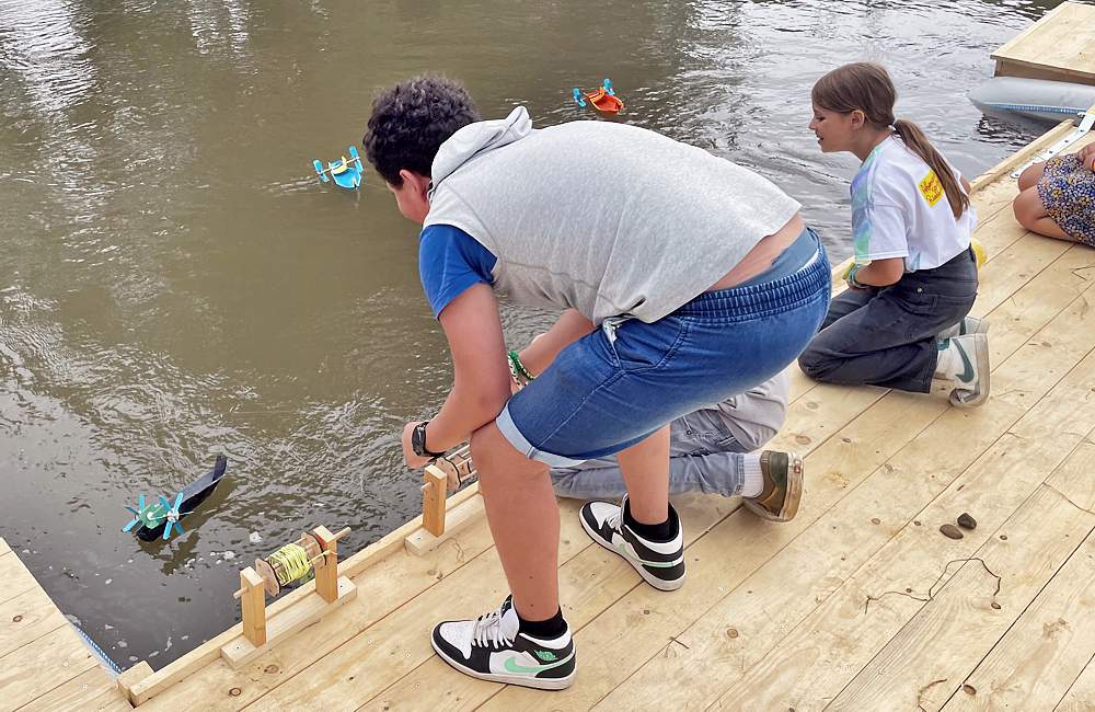 Ein Junge und ein Mädchen lassen vom Steg aus ihre fertigen Schwimmkörper zur Untersuchung der Wasserqualität ins Wasser. Die Schwimmkörper sind an langen Schnüren befestigt, so dass wieder eingezogen werden können.