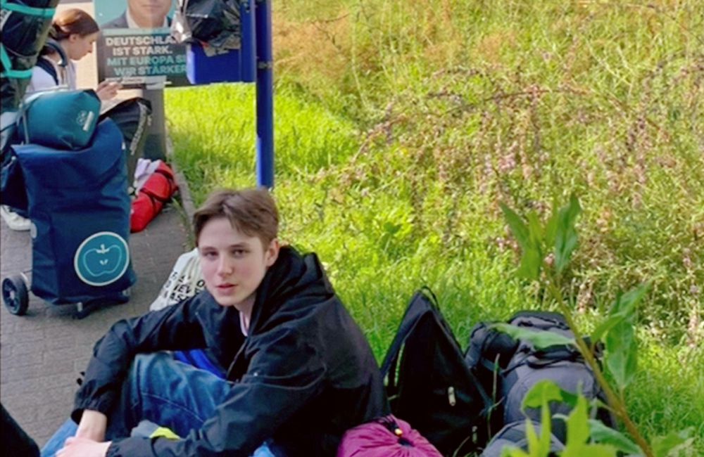 Die Teilnehmer sind unterwegs in Deutschland, sie kommen im Moment nicht weiter. Ihre Rucksäcke haben sie auf dem Gehweg abgestellt.