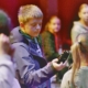 Ein Junge in blauer Jacke hält ein schwarzes Gerät mit roten Leuchten in der rechten Hand und blickt konzentriert darauf. Um ihn herum stehen weitere Kinder.